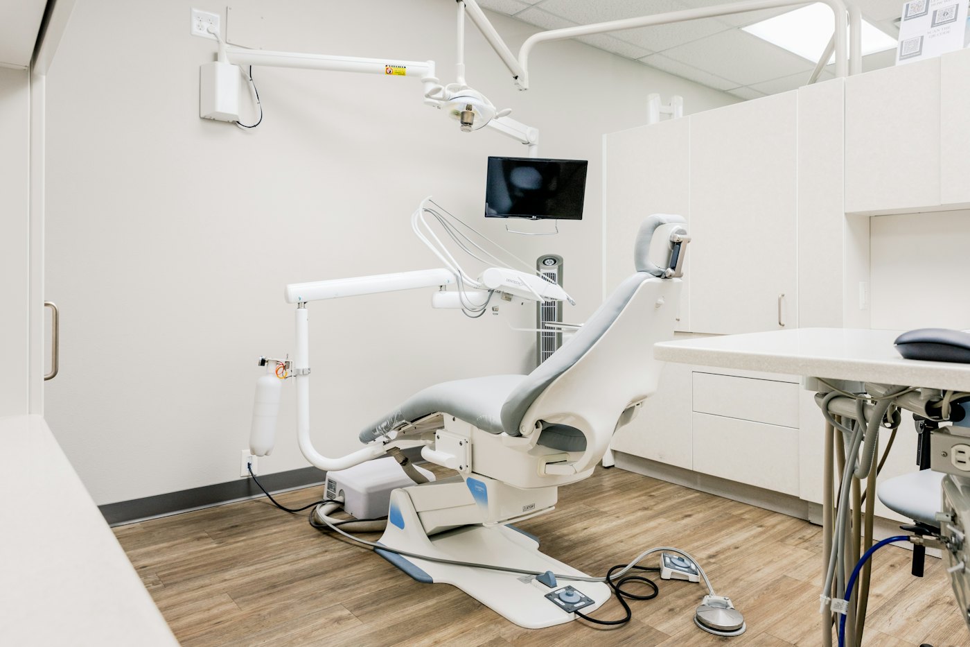 An empty dental treatment room with the chair and monitor switched off
